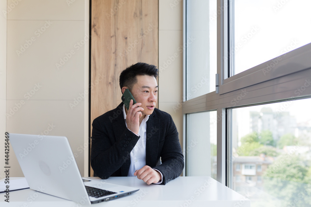 Serious asian business businessman uses cellphone to communicate with colleagues while sitting in modern office Serious asian business businessman uses cellphone to communicate with colleagues while sitting in modern office