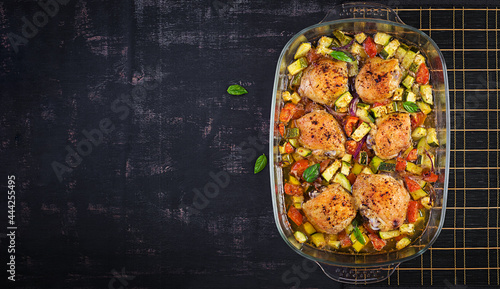 Baked chicken thighs, zucchini and vegetables in a baking dish on a dark table. Top view, overhead