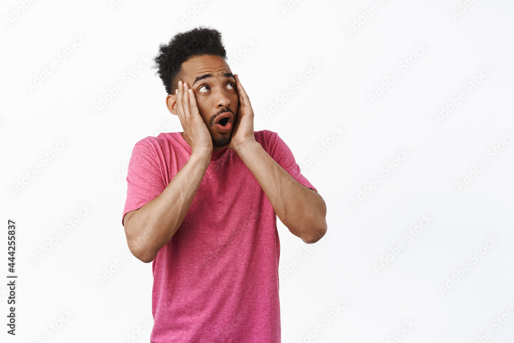 Shocked african american guy gasp, scream and look scared at upper right corner, frustrated by smth, frightened of logo aside, standing in pink t-shirt against white background Shocked african american guy gasp, scream and look scared at upper right corner, frustrated by smth, frightened of logo aside, standing in pink t-shirt against white background