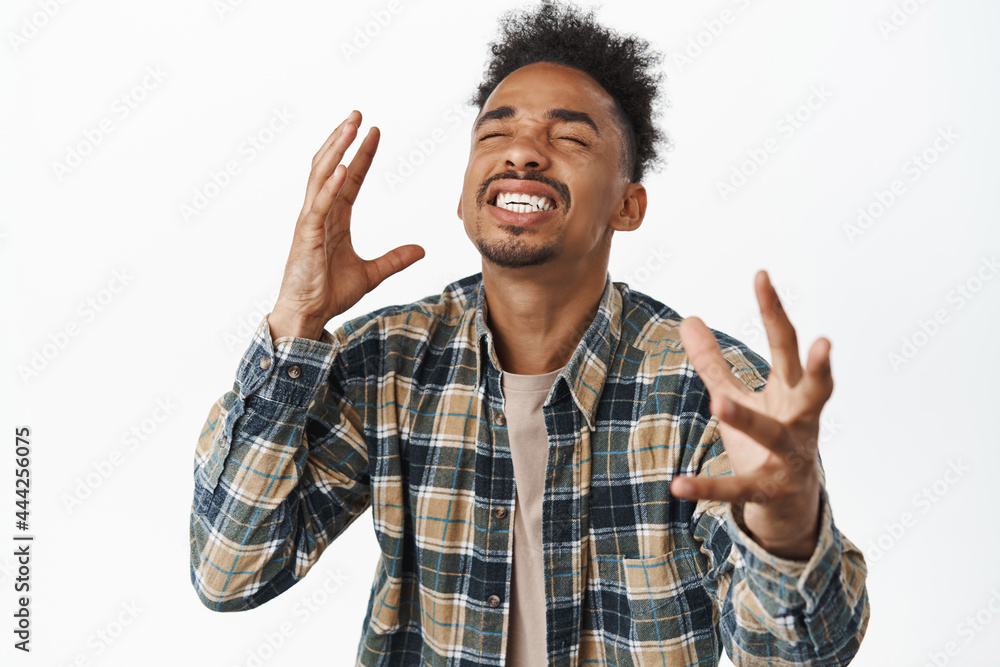 Image of happy and relieved african american man rejoicing, feeling pleasure and delighted, smiling with joy and closed eyes, shaking hands, achieve goal and celebrate, white background Image of happy and relieved african american man rejoicing, feeling pleasure and delighted, smiling with joy and closed eyes, shaking hands, achieve goal and celebrate, white background