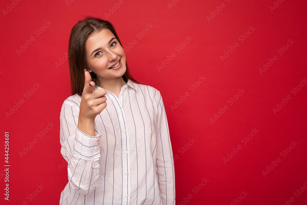 Young smiling beautiful brunette woman with sincere emotions isolated on background wall with copy space wearing casual white shirt and pointing finger at camera. Positive concept Young smiling beautiful brunette woman with sincere emotions isolated on background wall with copy space wearing casual white shirt and pointing finger at camera. Positive concept