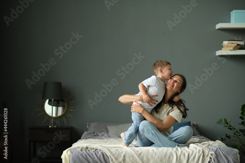mother hugs with her toddler little son on a bed together. Family moments, children care. Motherhood, maternity leave concept