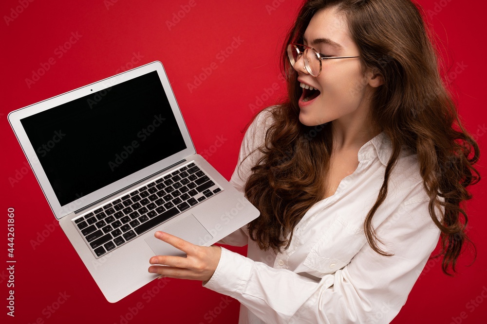 Close-up portrait of overjoyed Beautiful smiling happy young woman holding computer laptop looking at netbook having fun wearing casual smart clothes isolated over wall background Close-up portrait of overjoyed Beautiful smiling happy young woman holding computer laptop looking at netbook having fun wearing casual smart clothes isolated over wall background