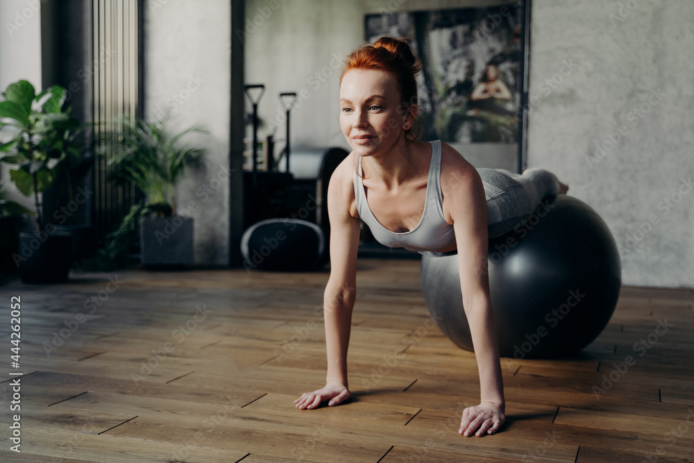 Fit woman balancing on exercise ball in fitness studio during pilates workout Fit woman balancing on exercise ball in fitness studio during pilates workout