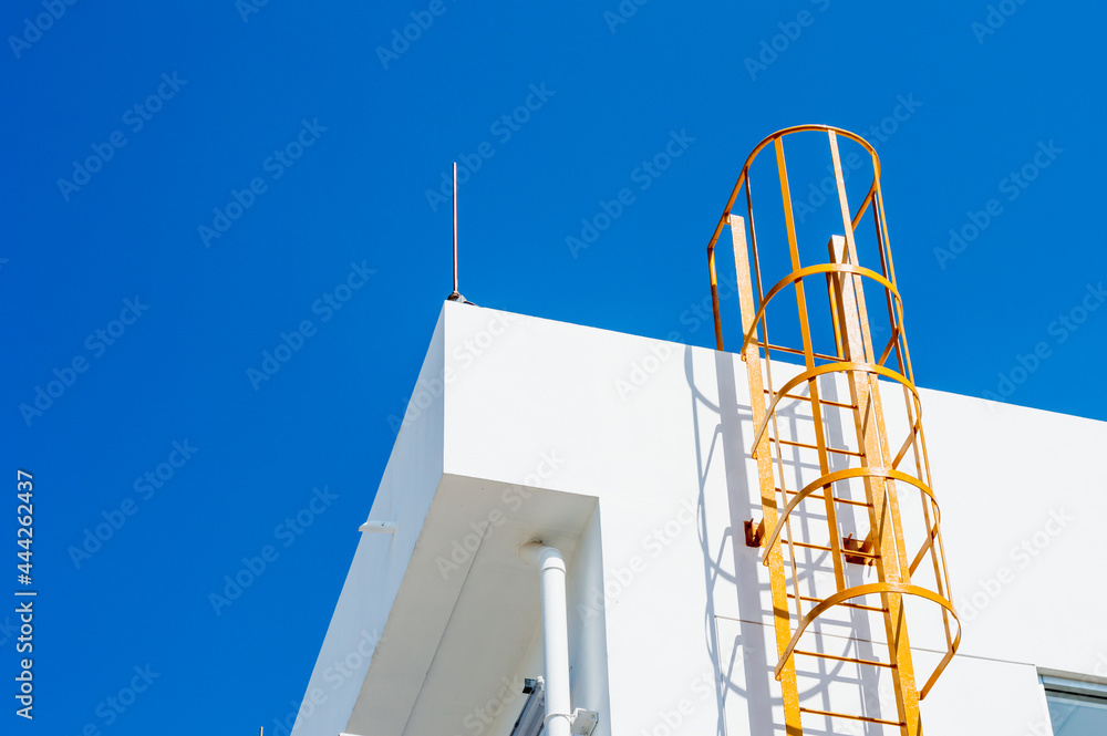 yellow metal ladder to roof (fire escape) on a white wall of building