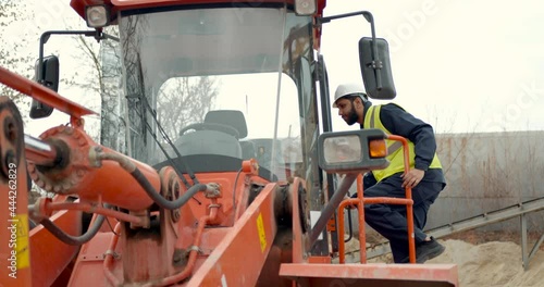 Man in hardhat entering tractor at building site