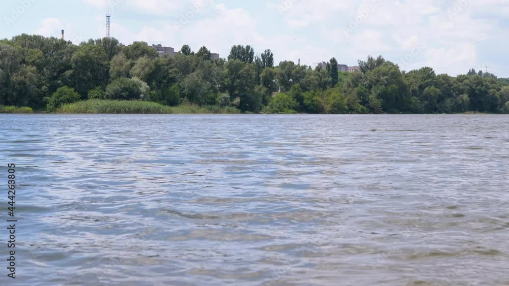 Slow Flow of Running Water in a Full Flowing River. Abundant stream of water, panoramic view, shore with green trees. Beautiful nature in summer. City Beach. 4K. Close up. Slow Flow of Running Water in a Full Flowing River. Abundant stream of water, panoramic view, shore with green trees. Beautiful nature in summer. City Beach. 4K. Close up.