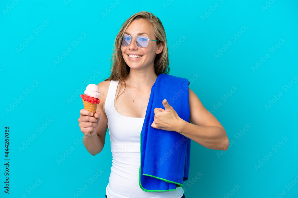 Young caucasian woman holding ice cream and wearing a beach towel isolated on blue background with thumbs up because something good has happened Young caucasian woman holding ice cream and wearing a beach towel isolated on blue background with thumbs up because something good has happened