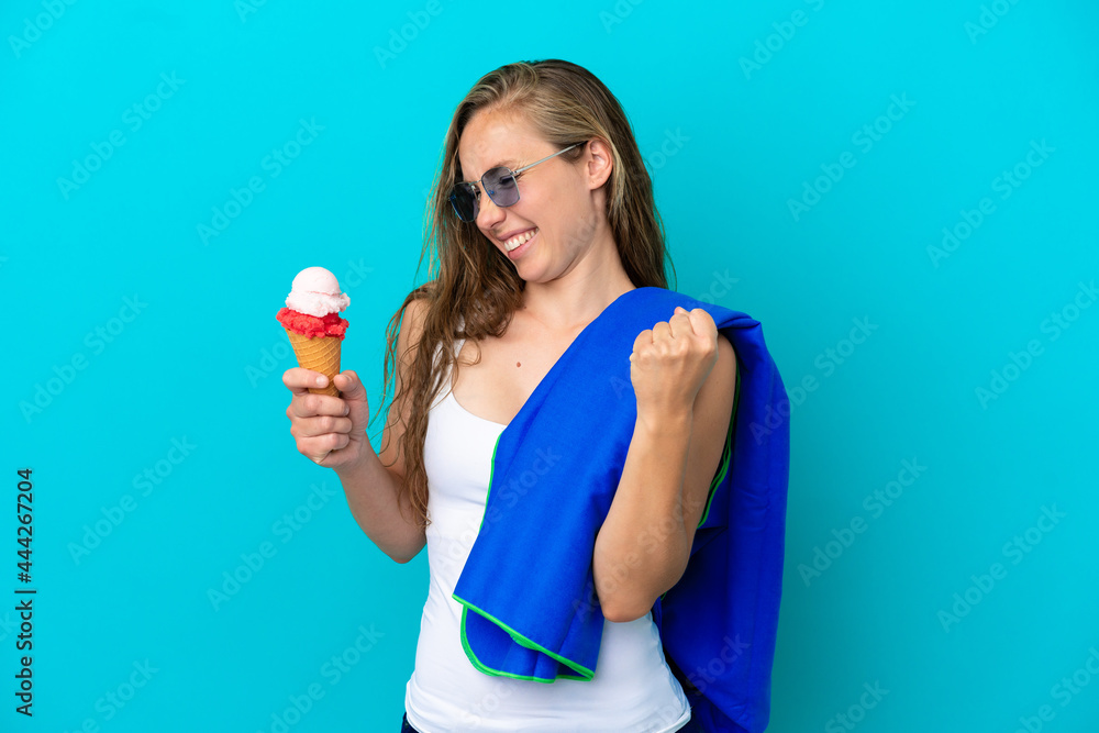 Young caucasian woman holding ice cream and wearing a beach towel isolated on blue background celebrating a victory Young caucasian woman holding ice cream and wearing a beach towel isolated on blue background celebrating a victory