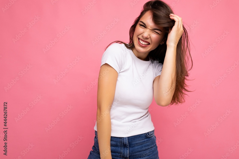 Photo portrait of young beautiful smiling hipster brunette woman in white t-shirt with mockup. Sexy carefree female person posing isolated near pink wall with empty space in studio. Positive model