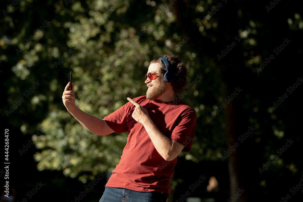 nordic man with beard in the park taking a self-portrait with his cell phone