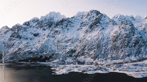 Breathtaking bird's eye view of majestic fjord mountains covered with snow in winter. Aerial view of scenery rock peaks, picturesque beautiful nature landscape. Lofoten Island surrounds by Nordic sea