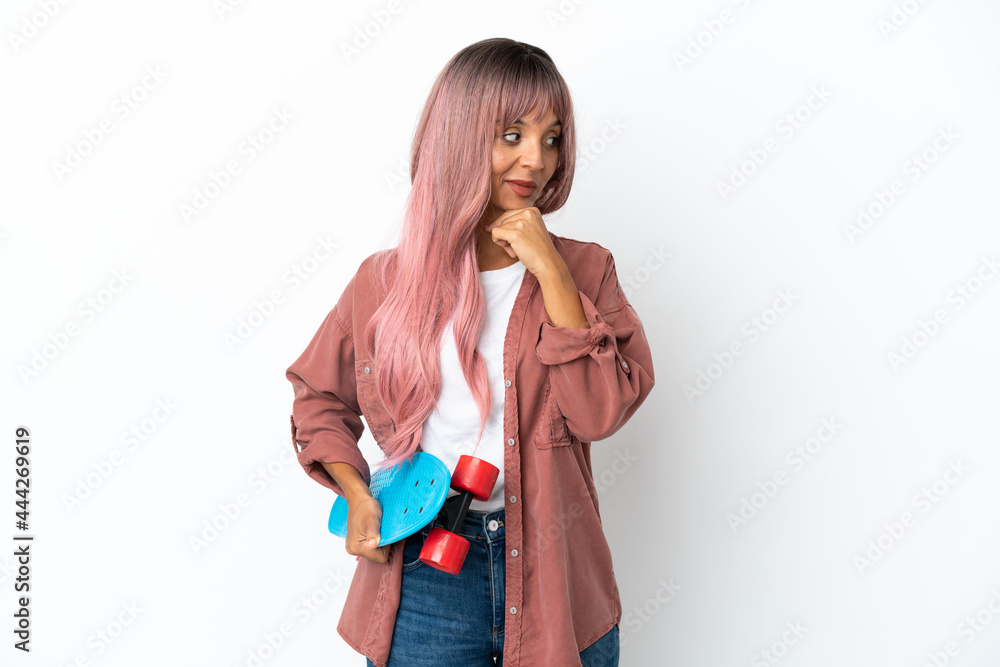 Young mixed race woman with pink hair isolated on white background with a skate and looking lateral Young mixed race woman with pink hair isolated on white background with a skate and looking lateral