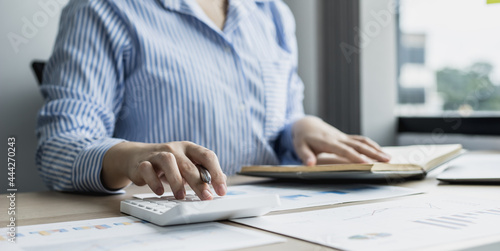 A businesswoman presses on a white calculator and looks at the numbers from a notebook she notes during a finance department meeting to check the accuracy of the numbers on the report. Finance concept