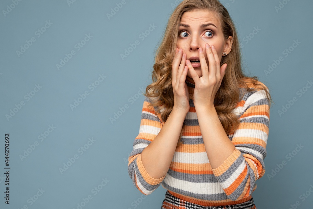 Young blond pretty curly woman with sincere emotions wearing striped jersey isolated on blue background with empty space and covering eyes scared and woried female person Young blond pretty curly woman with sincere emotions wearing striped jersey isolated on blue background with empty space and covering eyes scared and woried female person