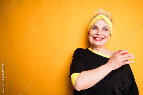 Happy elderly woman in black t-shirt relaxes back and shoulder muscles with massage ball