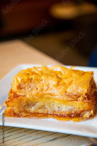 Delicious Greek sweet pastry named Galaktoboureko, made of semolina custard in filo, served with honey in white plate.