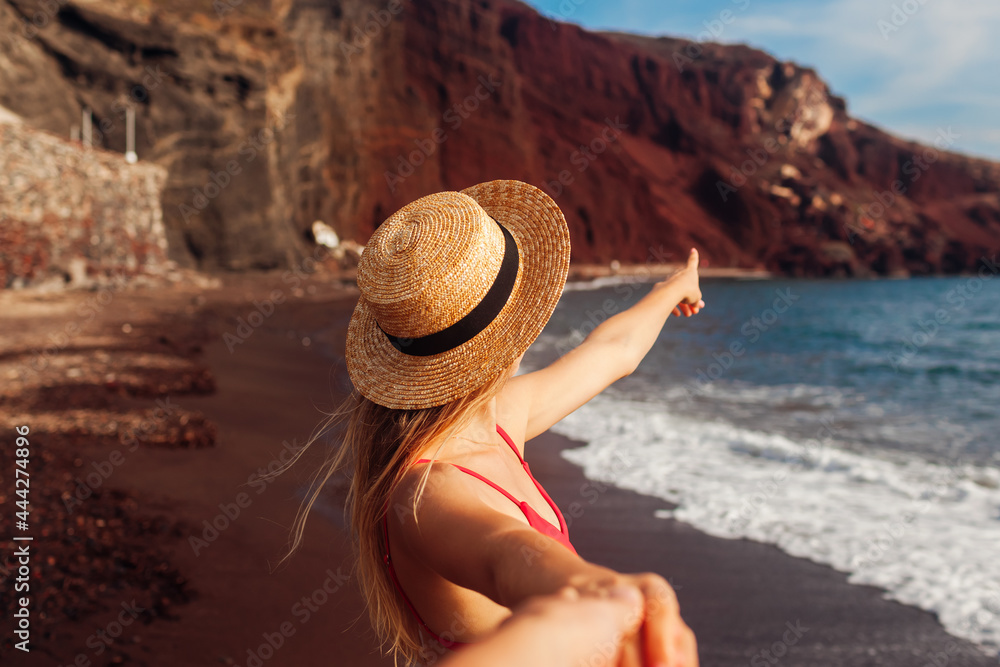 Woman in bikini walking on Red beach on Santorini, Greece. Girl holds hand of man pointing on landscape
