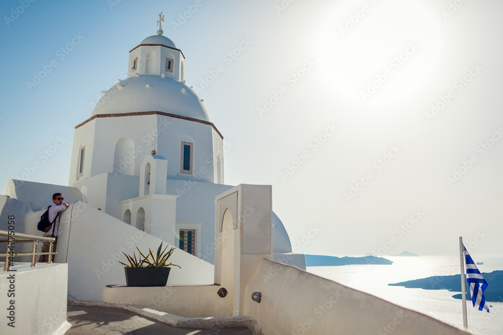 Man tourist enjoying traditional architecture walking by white church on Santorini island with sea landscape in Fira