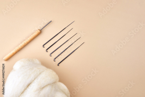 Needles and skein of wool for felting on a beige background.