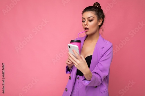 Young sexy positive woman isolated over pink background with copy space holding coffee to take away and a mobile phone