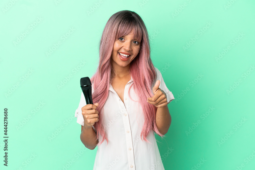 Young mixed race singer woman with pink hair isolated on green background with thumbs up because something good has happened Young mixed race singer woman with pink hair isolated on green background with thumbs up because something good has happened