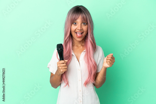 Young mixed race singer woman with pink hair isolated on green background celebrating a victory in winner position