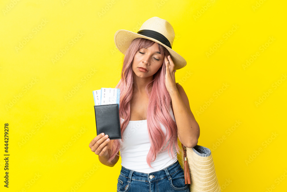 Young mixed race woman holding passport and beach bag isolated on yellow background with headache Young mixed race woman holding passport and beach bag isolated on yellow background with headache
