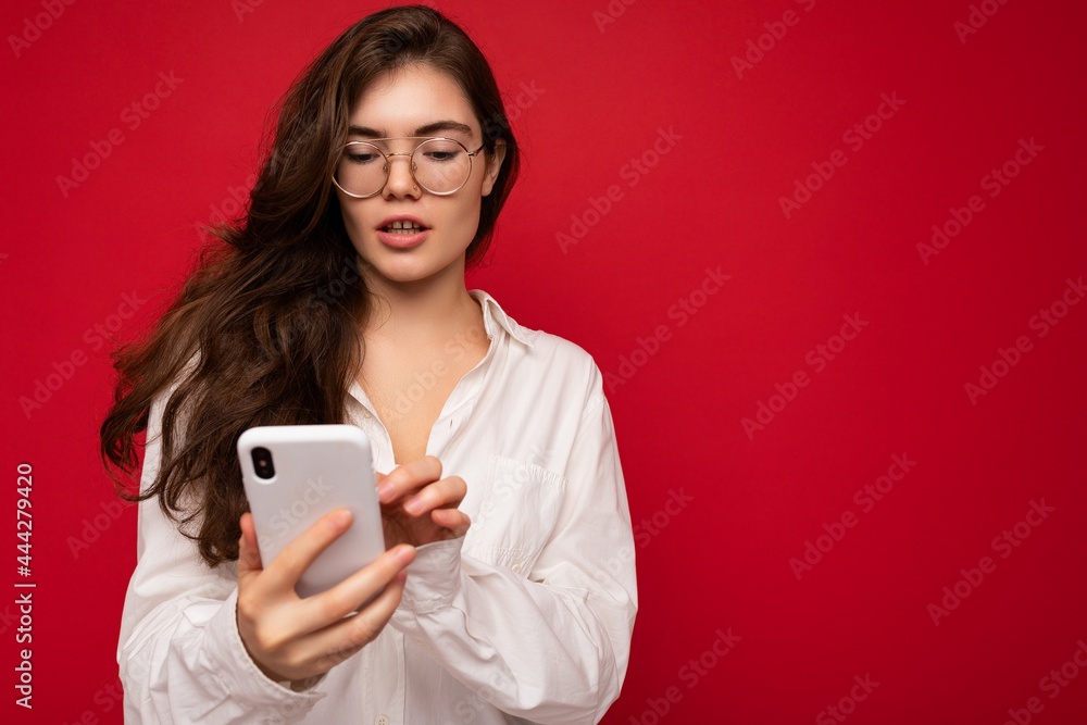 Beautiful young woman wearing casual clothes standing isolated over background surfing on the internet via phone looking at mobile screen Beautiful young woman wearing casual clothes standing isolated over background surfing on the internet via phone looking at mobile screen