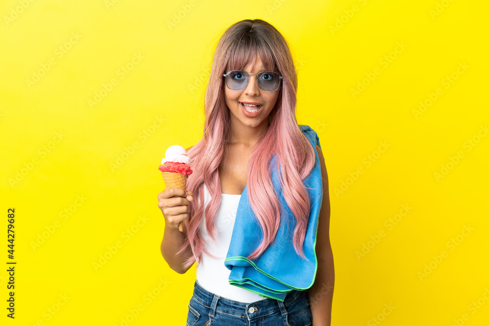 Young mixed race woman with pink hair holding ice cream isolated on yellow background with surprise facial expression Young mixed race woman with pink hair holding ice cream isolated on yellow background with surprise facial expression