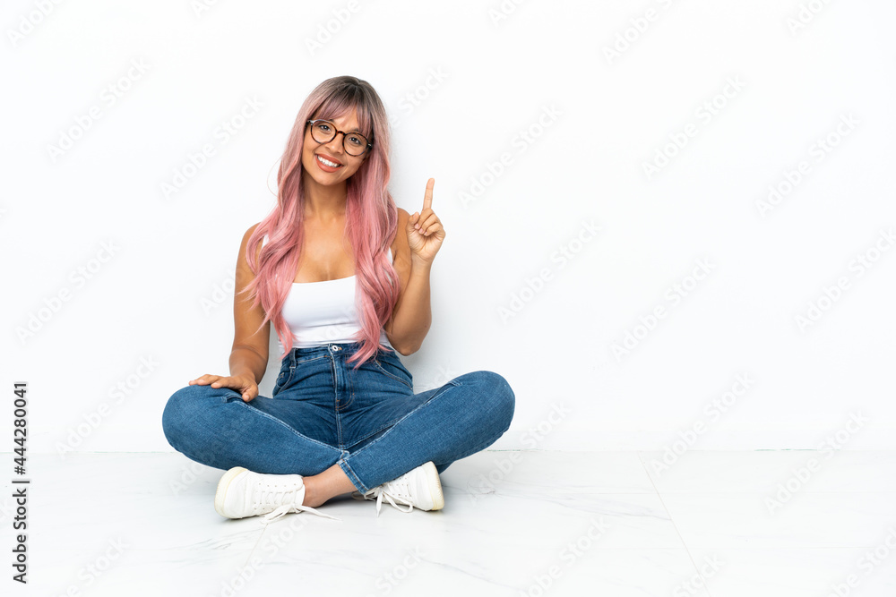 Young mixed race woman with pink hair sitting on the floor isolated on white background showing and lifting a finger in sign of the best Young mixed race woman with pink hair sitting on the floor isolated on white background showing and lifting a finger in sign of the best