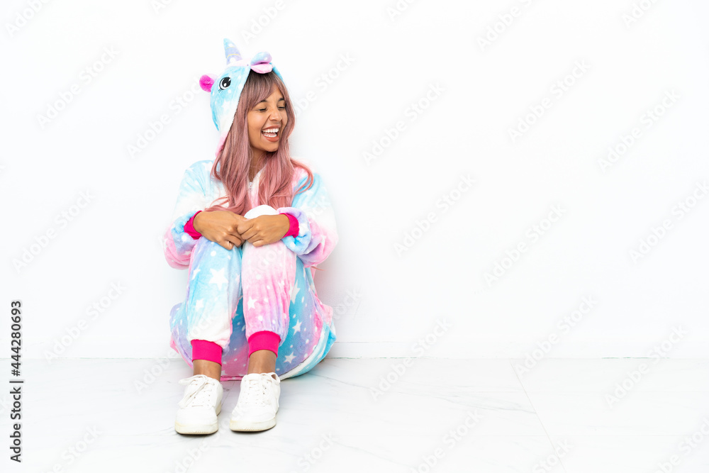 Young mixed race woman wearing a unicorn pajama sitting on the floor isolated on white background laughing in lateral position