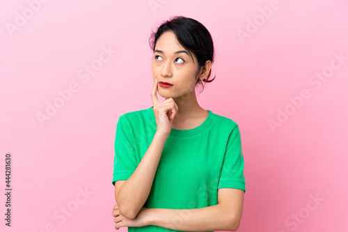Young Vietnamese woman isolated on pink background having doubts while looking up