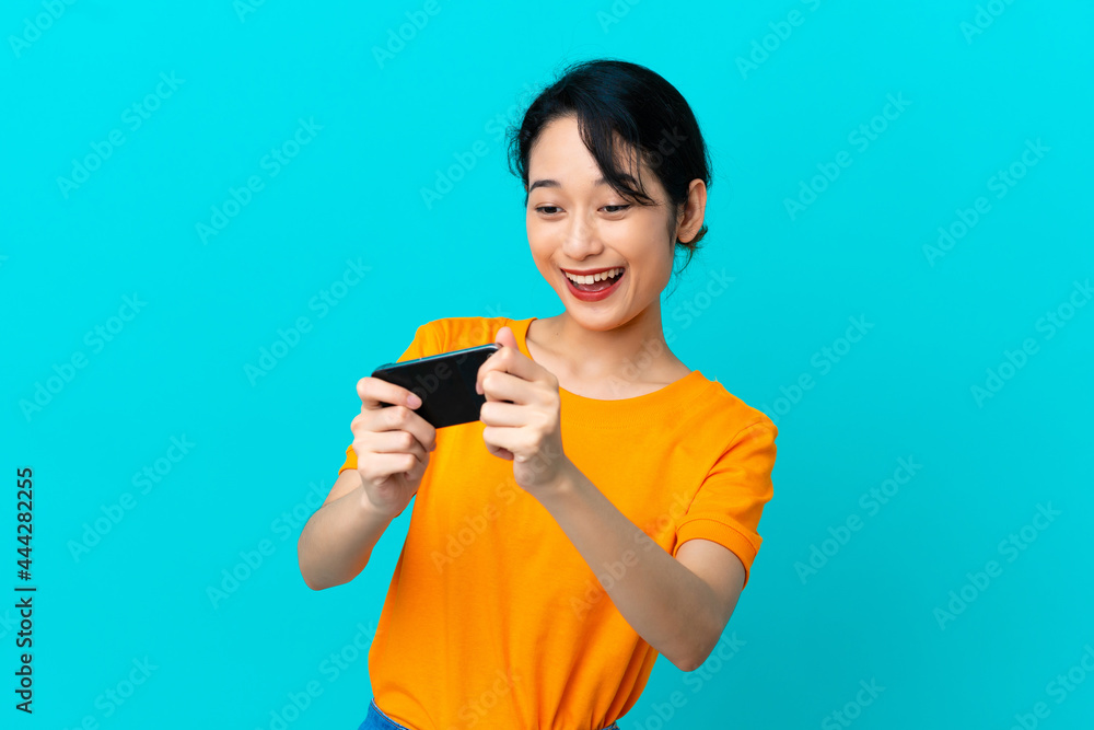 Young Vietnamese woman isolated on blue background playing with the mobile phone Young Vietnamese woman isolated on blue background playing with the mobile phone