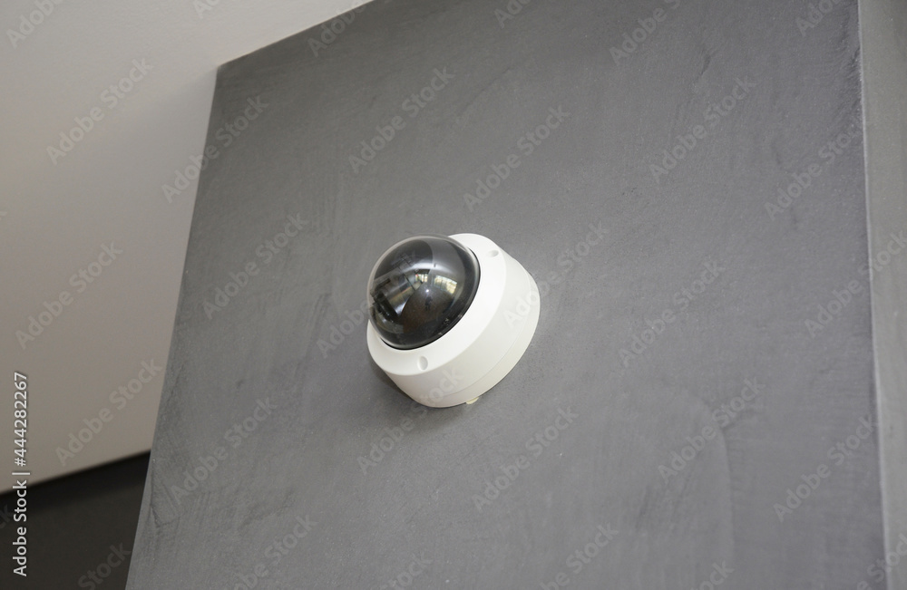 A close-up of a round security camera, security surveillance installed on a gray plastered wall inside a modern apartment. A close-up of a round security camera, security surveillance installed on a gray plastered wall inside a modern apartment.