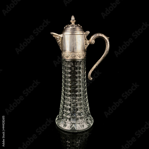 Antique crystal decanter with glass handle and metal neck against black background. Traditional wine jug, Vintage engraving