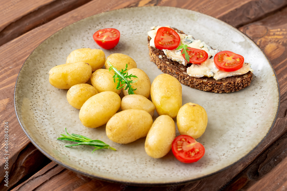Boiled young potatoes and cereal bread with blue cheese and tomatoes on a plate on a wooden background. Vegetarian food. Boiled young potatoes and cereal bread with blue cheese and tomatoes on a plate on a wooden background. Vegetarian food.