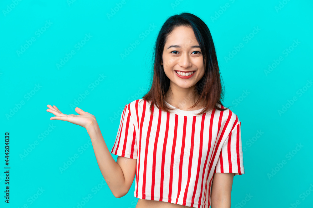 Young Vietnamese woman isolated on blue background holding copyspace imaginary on the palm to insert an ad Young Vietnamese woman isolated on blue background holding copyspace imaginary on the palm to insert an ad
