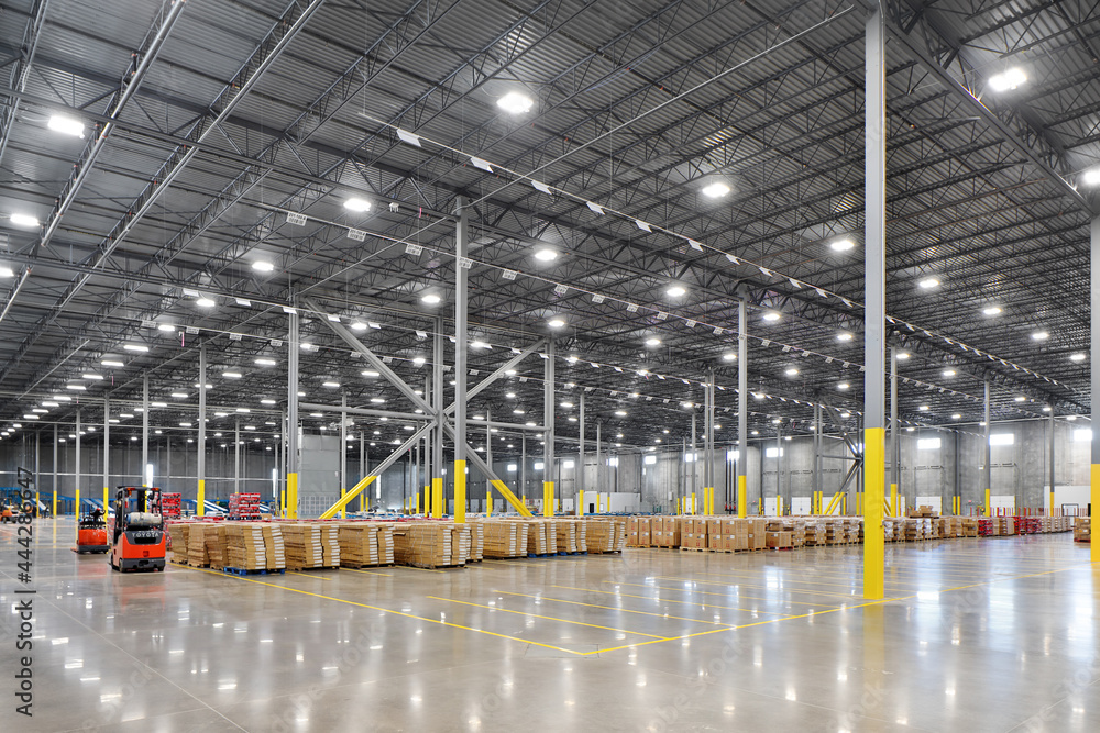 Interior of large warehouse industrial building with parked forklifts, shipping containers, and crates - obrazy, fototapety, plakaty 