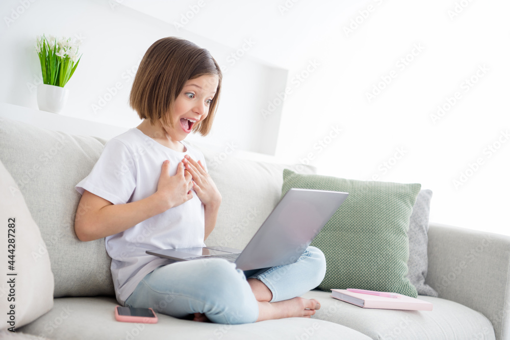 Portrait of attractive amazed girlish cheerful girl sitting on sofa watching film having fun free time at light white flat home indoors