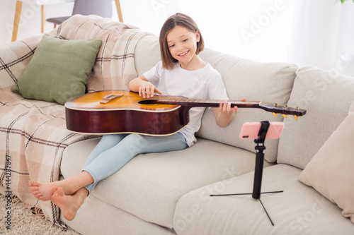 Full body photo of young cheerful girl happy positive smile online lesson learn play guitar sit sofa home