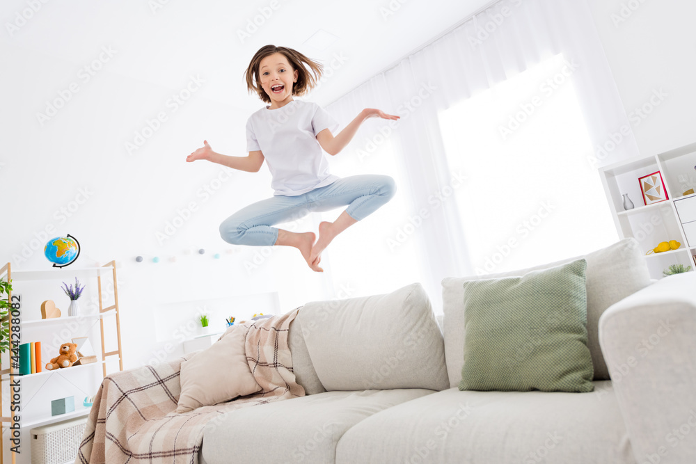 Full length photo of young cheerful little girl happy positive smile jump couch balance fly weekend home Full length photo of young cheerful little girl happy positive smile jump couch balance fly weekend home