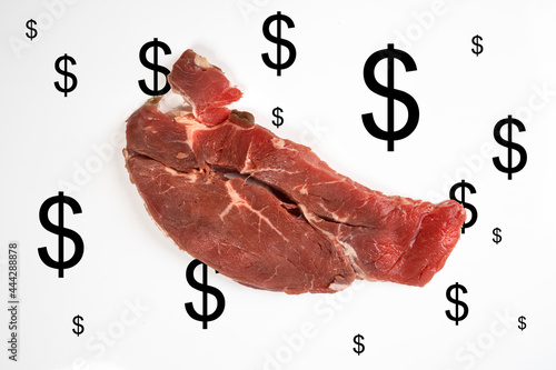 increase in the cost of meat. A roast beef steak with some dollar signs on a white surface photo