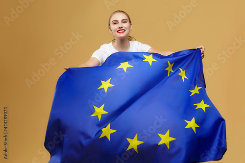 attractive blonde poses with the flag of the European Union. photo shoot in the studio on a yellow background