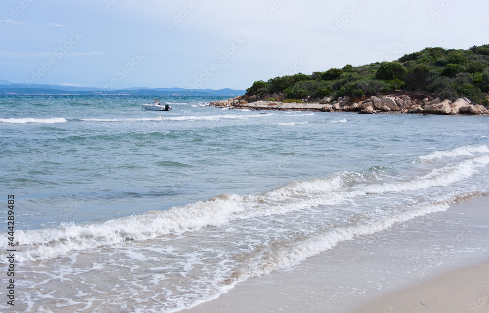 view of the beach and sea with little waves and boat , resort on Sardinia island