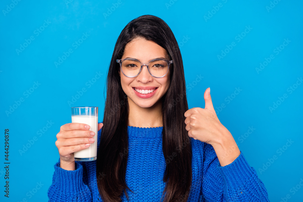Photo portrait young girl wearing glasses keeping milk glass showing thumb-up gesture isolated vivid blue color background Photo portrait young girl wearing glasses keeping milk glass showing thumb-up gesture isolated vivid blue color background