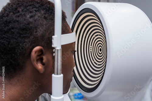 Black woman in optometry cabinet using a modern corneal topographer