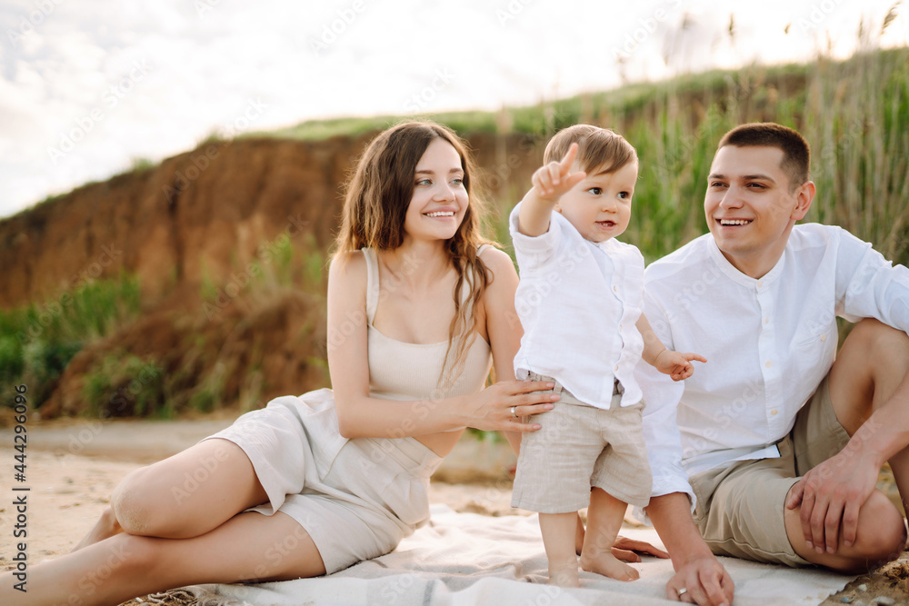 Cheerful young family with little baby boy spending time together on the beach. Father, mother and child against the background of the blue sea and sky. Family, childhood, active lifestyle concept. Cheerful young family with little baby boy spending time together on the beach. Father, mother and child against the background of the blue sea and sky. Family, childhood, active lifestyle concept.