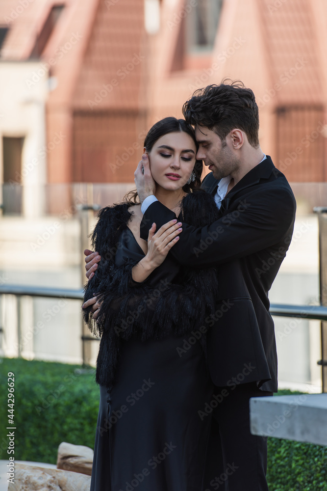 man hugging woman in black dress and faux fur jacket on terrace of restaurant man hugging woman in black dress and faux fur jacket on terrace of restaurant