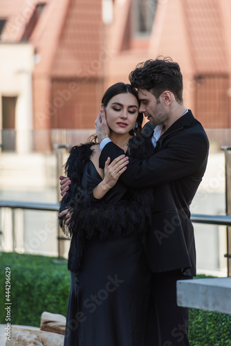 man hugging woman in black dress and faux fur jacket on terrace of restaurant
